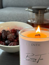 Load image into Gallery viewer, Close up of flame lit on a wooden wick on a Berry Tea cosy candle in front of a bowl of mixed berries and a teapot.
