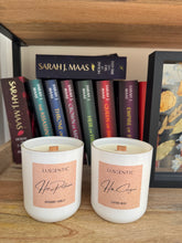 Load image into Gallery viewer, Two candles labeled 'Luscentic' on a wooden surface with books by Sarah J. Maas in the background.