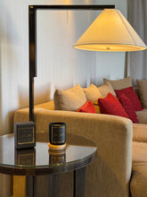 Load image into Gallery viewer, Floor lamp with a beige shade on a glass table next to a beige sofa with red and beige pillows.