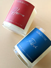 Load image into Gallery viewer, A red candle labeled &#39;Happiness&#39; lying down next to a blue candle labeled &#39;Refresh&#39;, both in glass jar containers.

