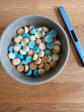 Load image into Gallery viewer, Gray bowl with colorful candy pieces on a wooden surface next to a blue electronic device.
