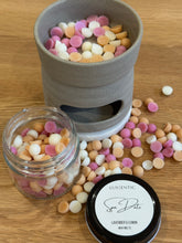 Load image into Gallery viewer, Wax melts in a container and jar on a wooden surface with a branded label.
